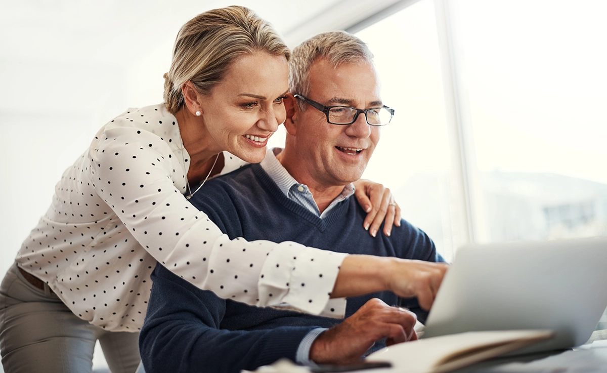 A man and woman investing on a laptop in a bright living area.