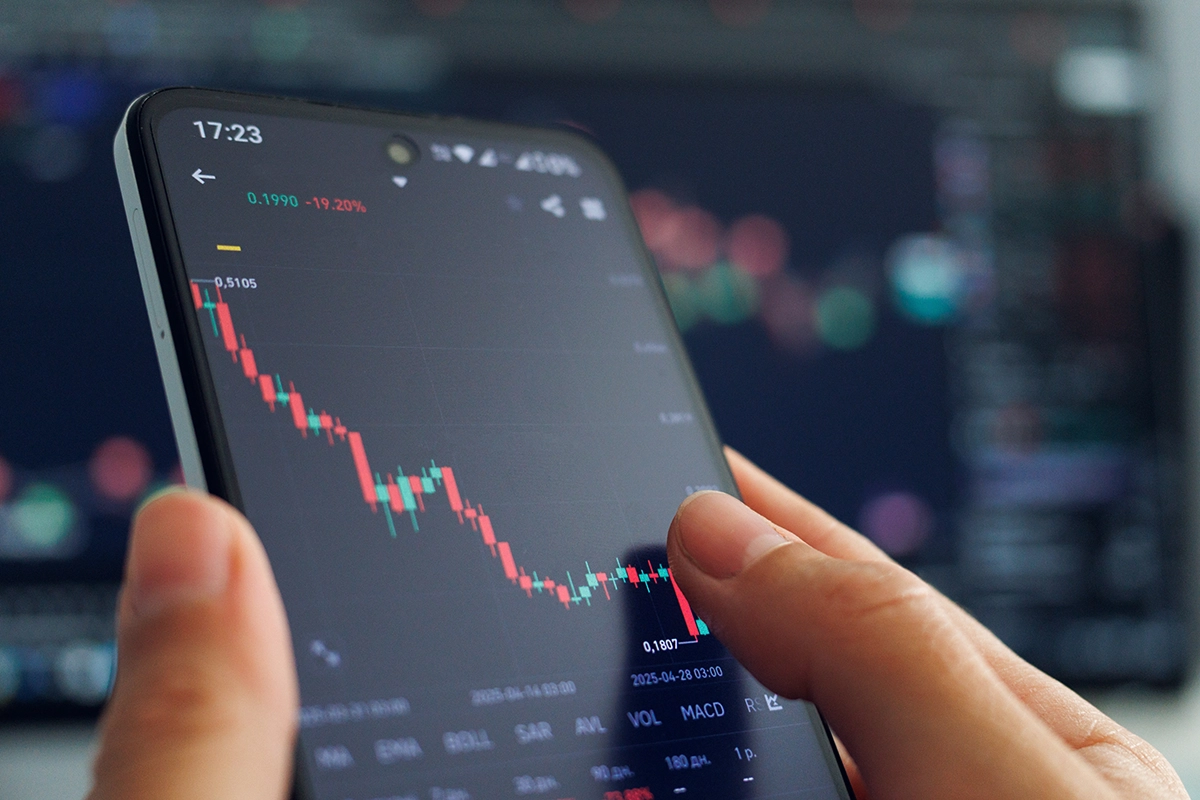 Someone holding a smartphone displaying an investment app with a stock market chart.