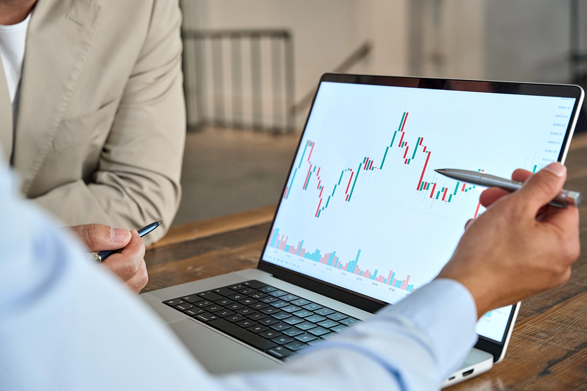Person explaining a fluctuating line graph on a laptop which is typical of the long-term movements of many types of investments.